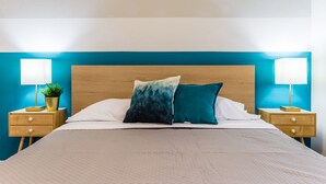 Ein ordentlich bezogenes Bett mit zwei Kissen, einem Holzkopfbrett und zwei Nachttischen mit Lampen und einer Pflanze.