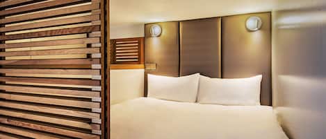 A hotel room with a wooden slat partition, a bed with white linens, and a headboard with two wall-mounted light fixtures.