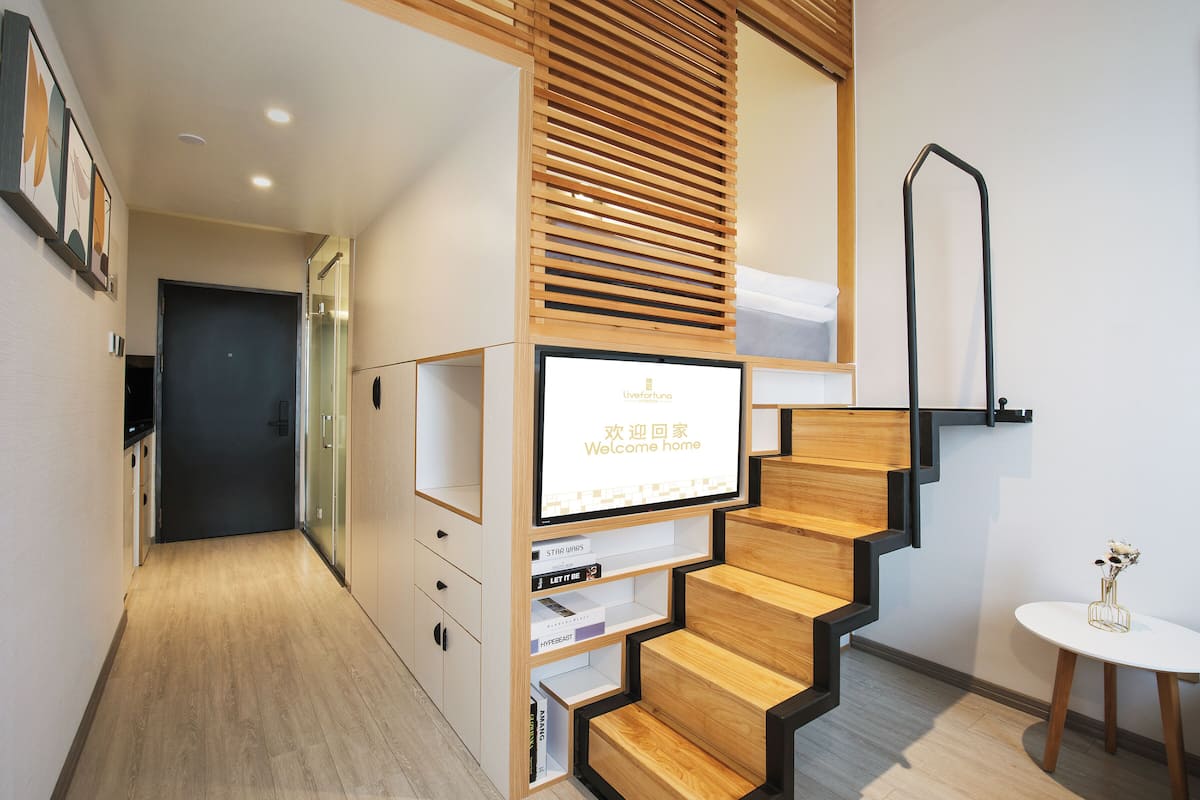 Ein modernes Hotelinnere mit einer Holztreppe, einem digitalen Empfangsbildschirm und minimalistischer Einrichtung.
