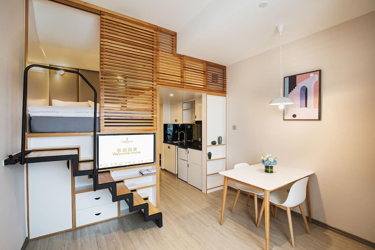 Ein kleines Hotelzimmer mit Etagenbett, Schreibtisch, Esstisch und einer Küchenzeile.