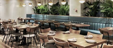 A restaurant with wooden tables and chairs, a blue cushioned bench, and hanging pendant lights.