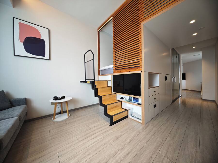 A modern living space with a staircase, a flat-screen TV, a small table, and a grey sofa.
