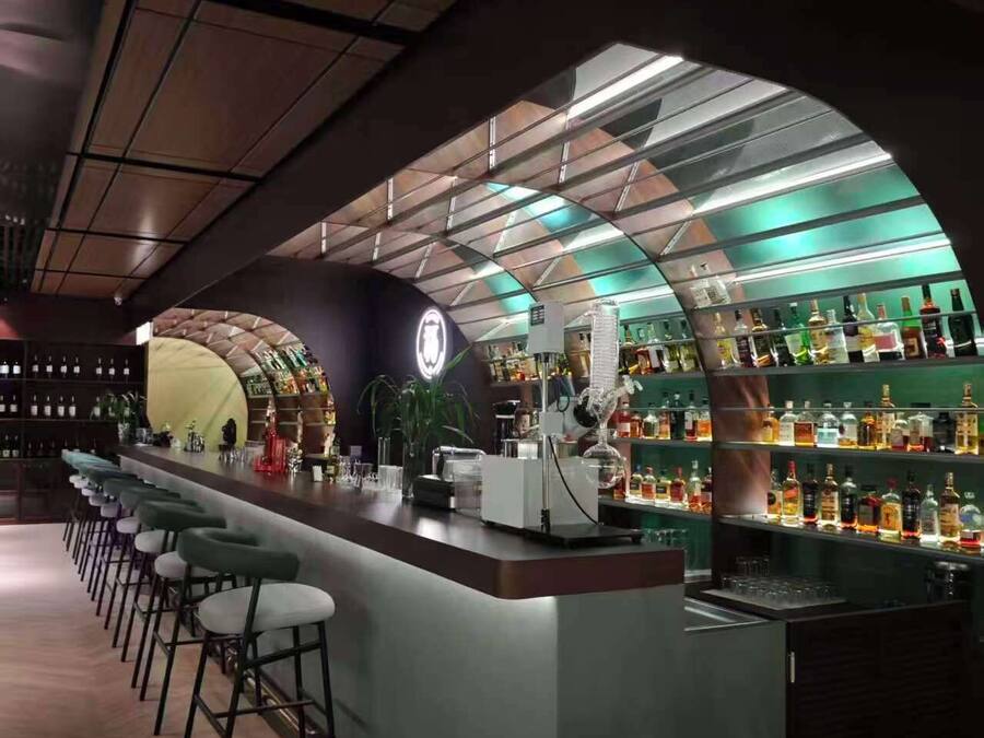 A bar area with a long counter, multiple stools, and shelves stocked with bottles.