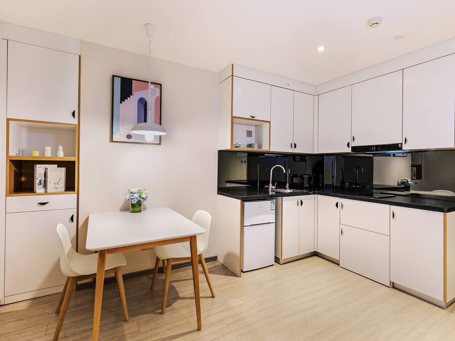 A modern kitchen with white cabinets, a black countertop, and a white dining table with chairs.