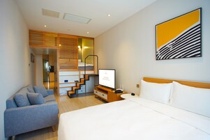 A modern hotel room with a bed, a sofa, a TV, and a staircase leading to an upper level.