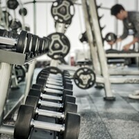 A gym with weightlifting equipment and a person working out in the background.