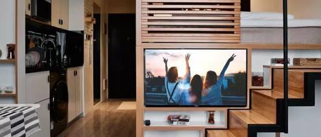 Una sala de estar moderna con un televisor montado en una pared de madera, una escalera y una zona de cocina.
