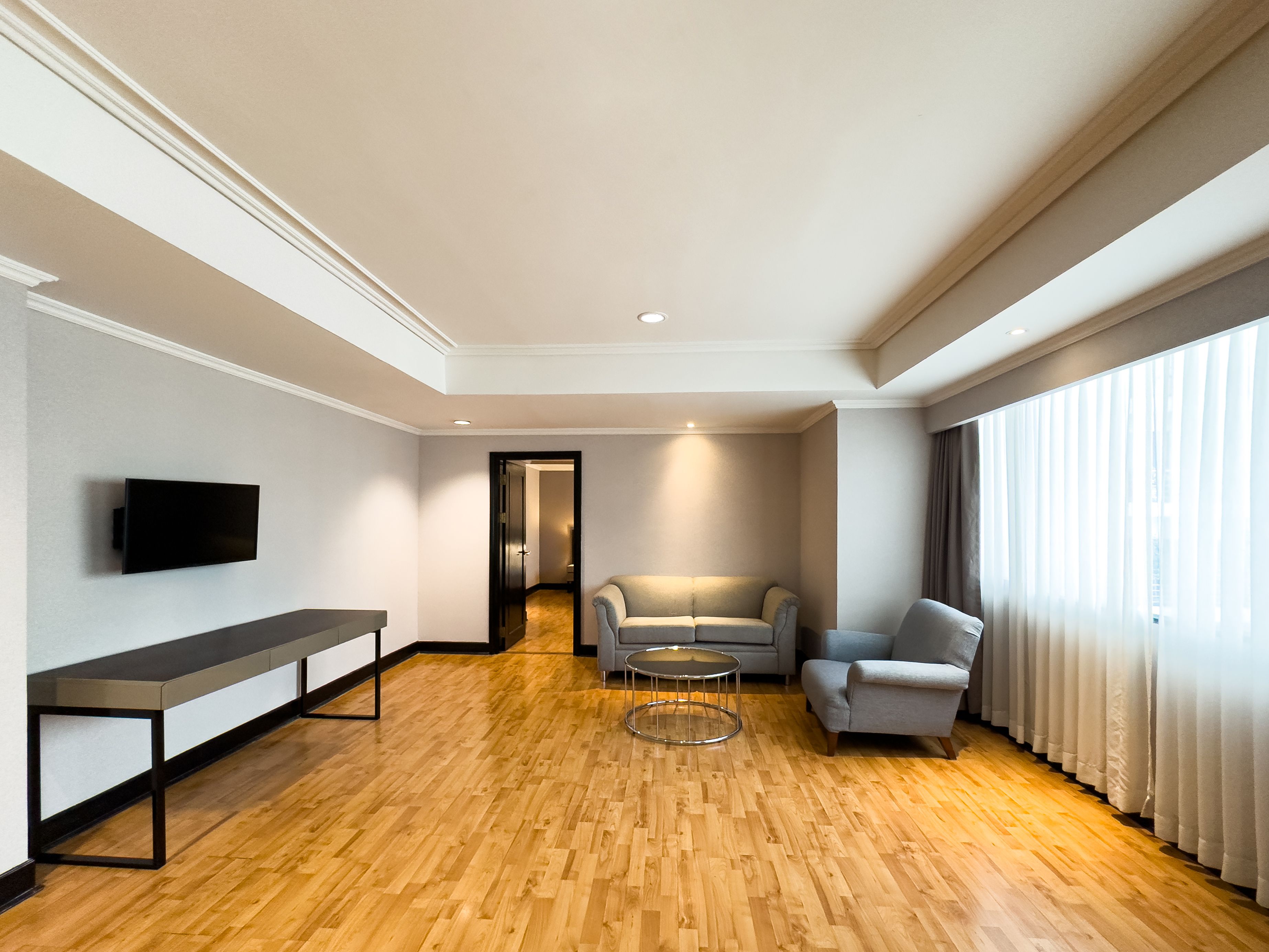 A modern living room with a wooden floor, a flat-screen TV mounted on the wall, a bench, two armchairs, and a coffee table.