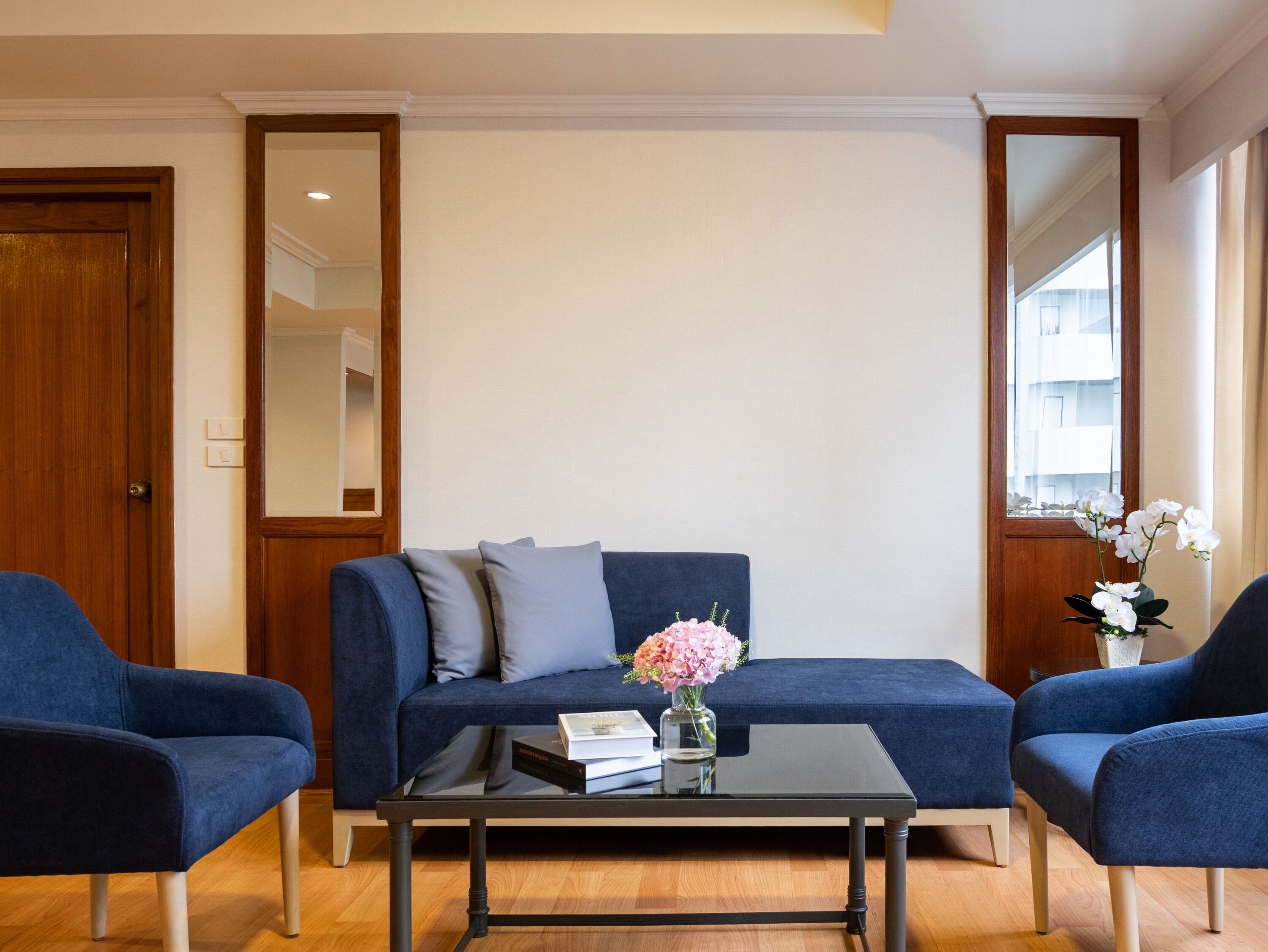 Ein Wohnzimmer mit einem blauen Sofa, zwei Sesseln, einem Couchtisch und einer Blumenvase.