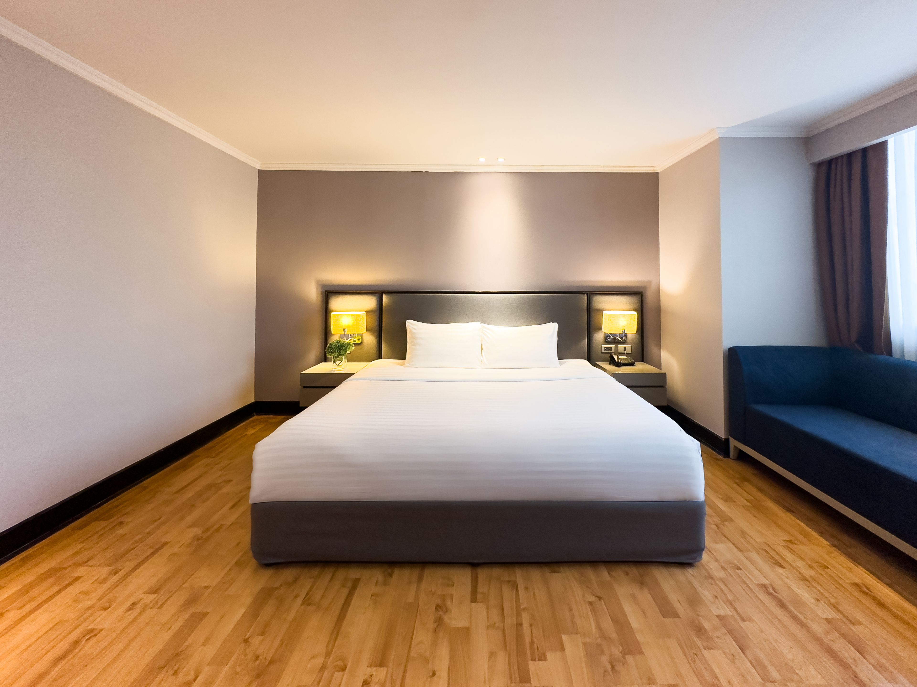 Habitación de hotel con una cama grande, dos mesitas de noche con lámparas, un sofá azul oscuro y una ventana con cortinas.