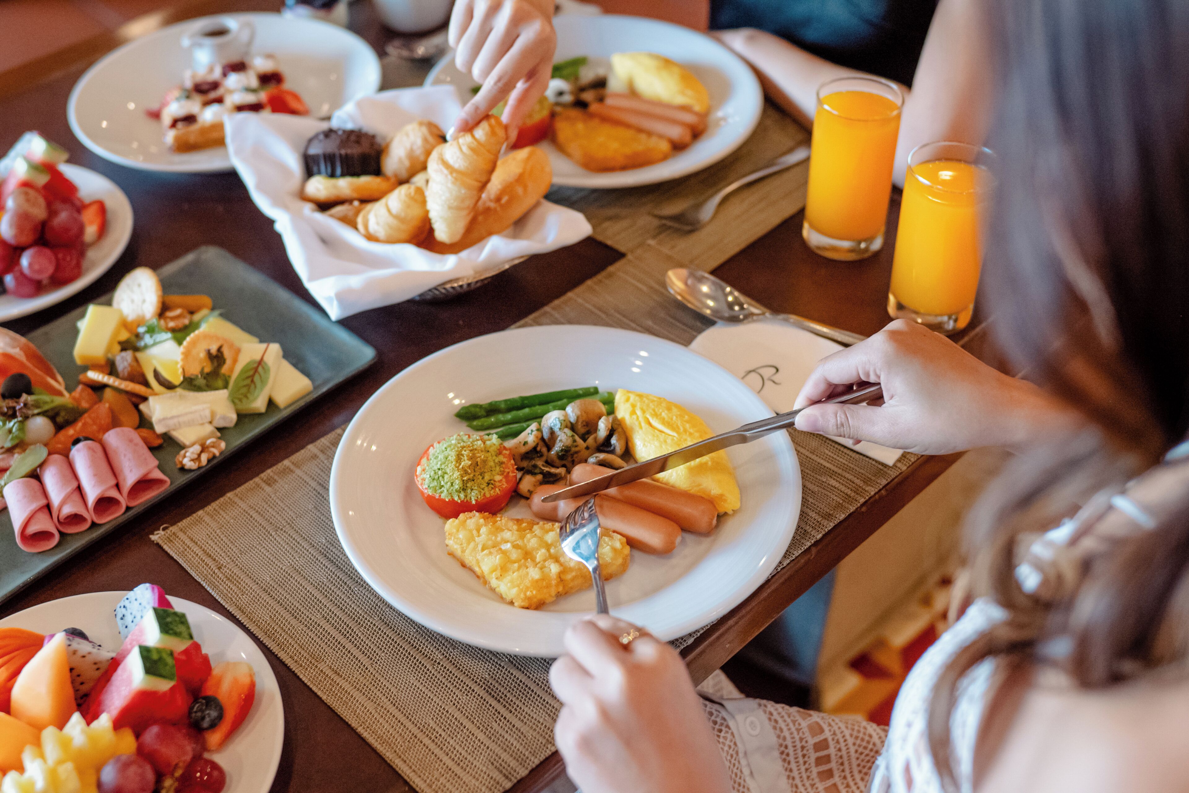 En frukostuppdukning med olika rätter, inklusive ägg, korv och frukt, på ett träbord.