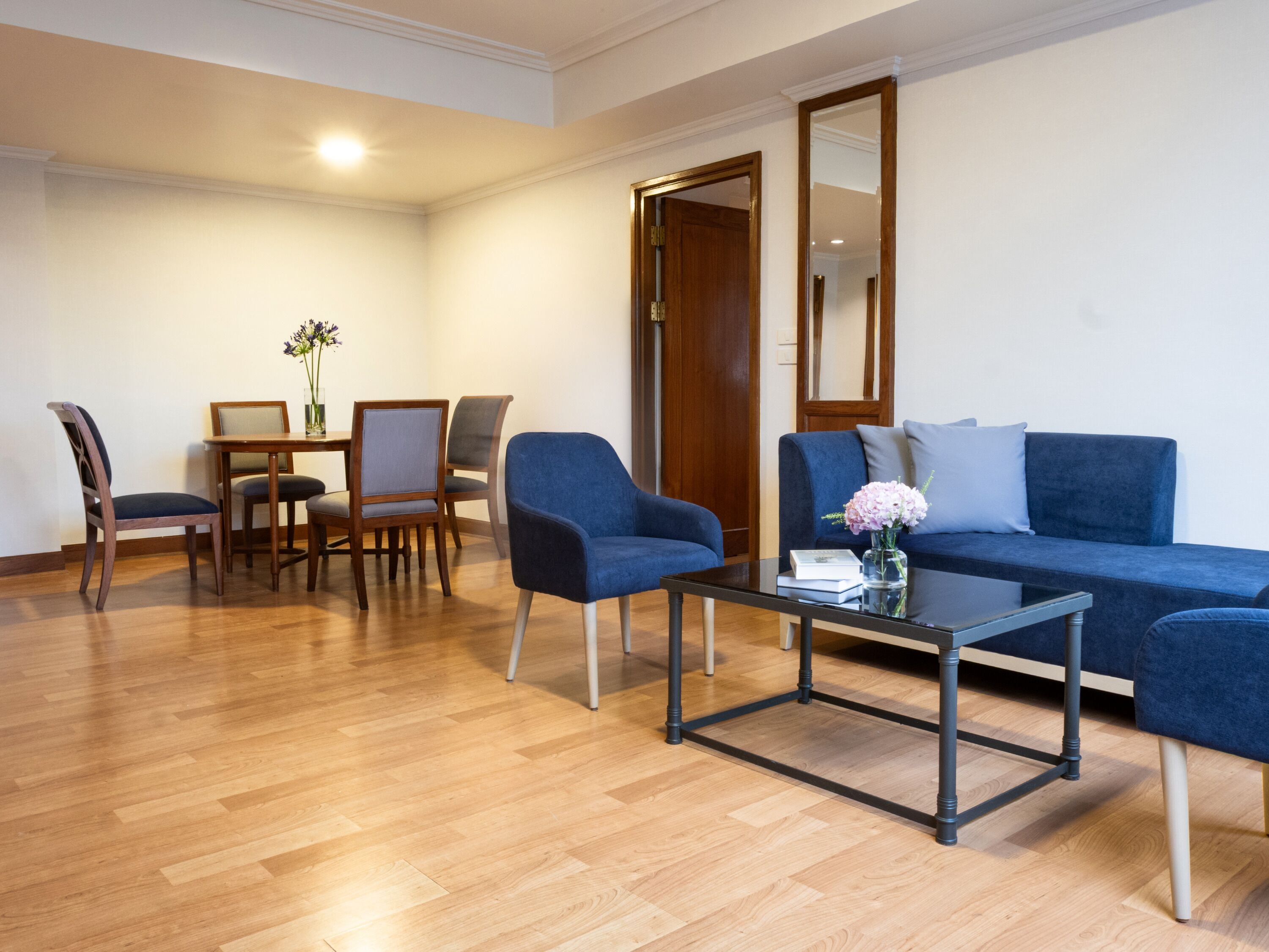 A modern living room with a blue sofa, a coffee table, and a dining area with chairs and a table.