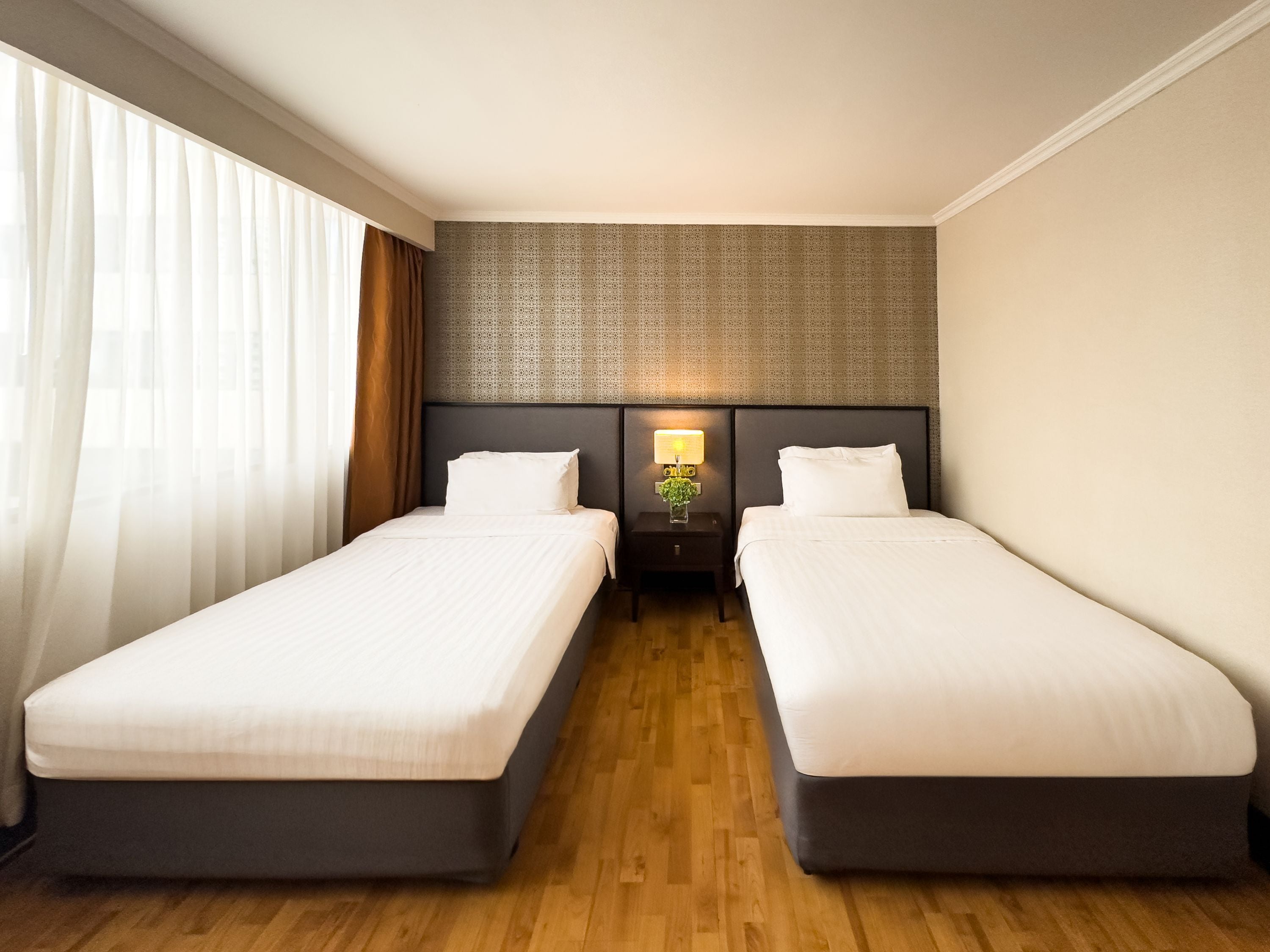 A hotel room with two single beds, a nightstand with a lamp, and a patterned headboard.