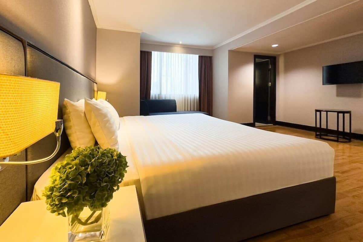 Habitación de hotel con una cama grande, una lámpara de noche, un televisor montado en la pared y una mesita.