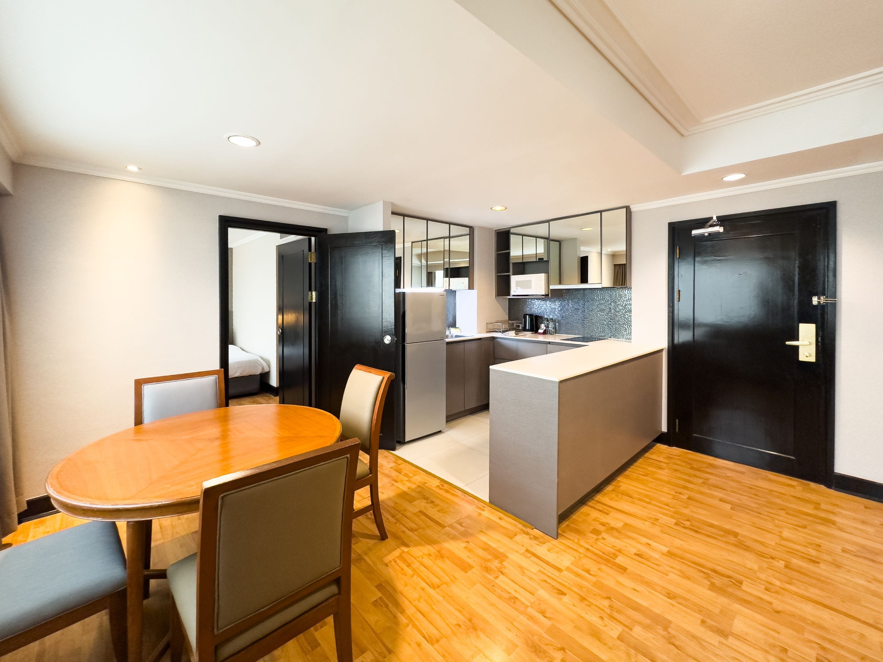 A modern hotel room with a wooden dining table, a kitchenette, and a separate sleeping area.