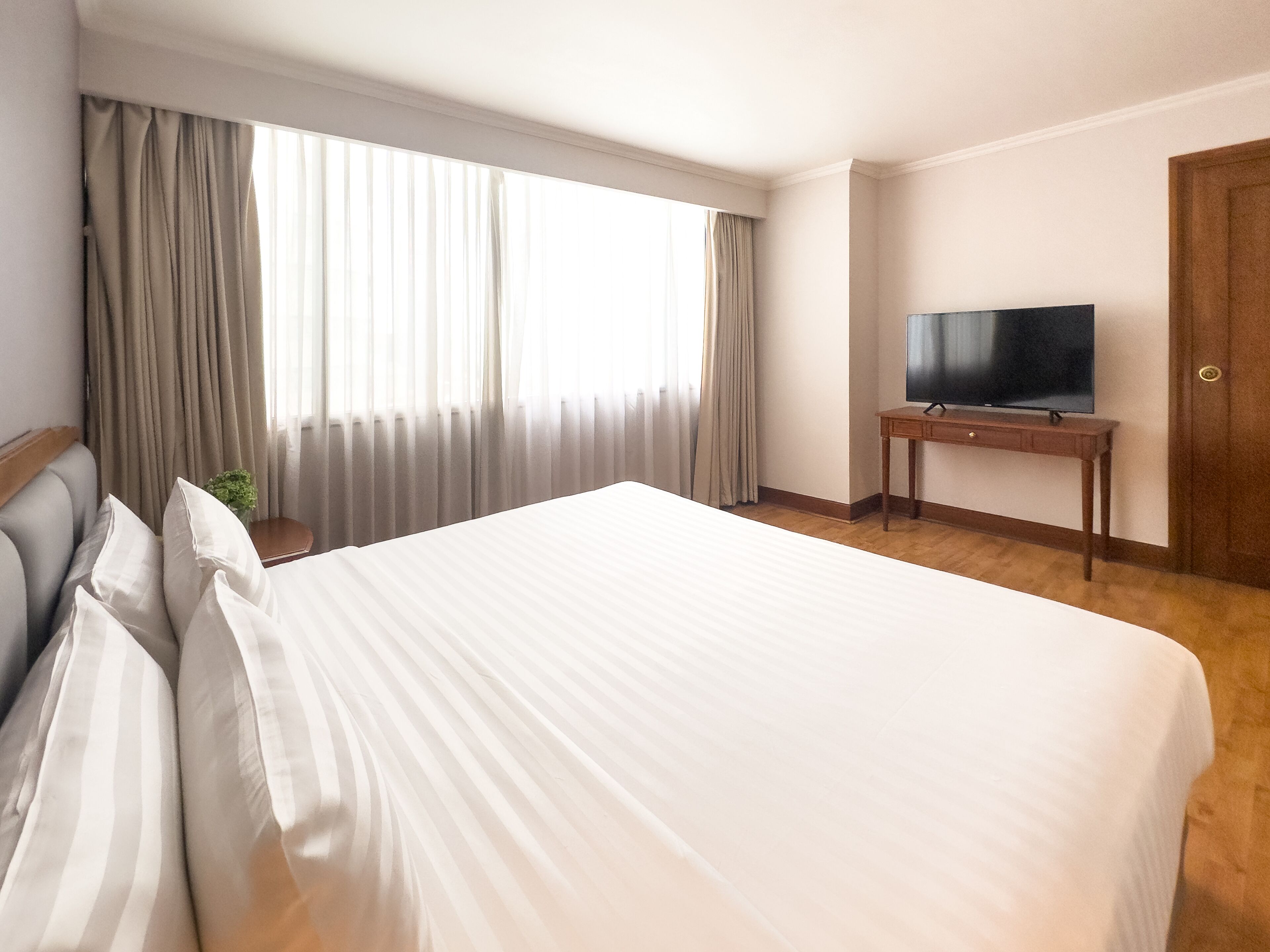 Una habitación de hotel con una cama grande, un televisor sobre un soporte de madera y una ventana con cortinas.