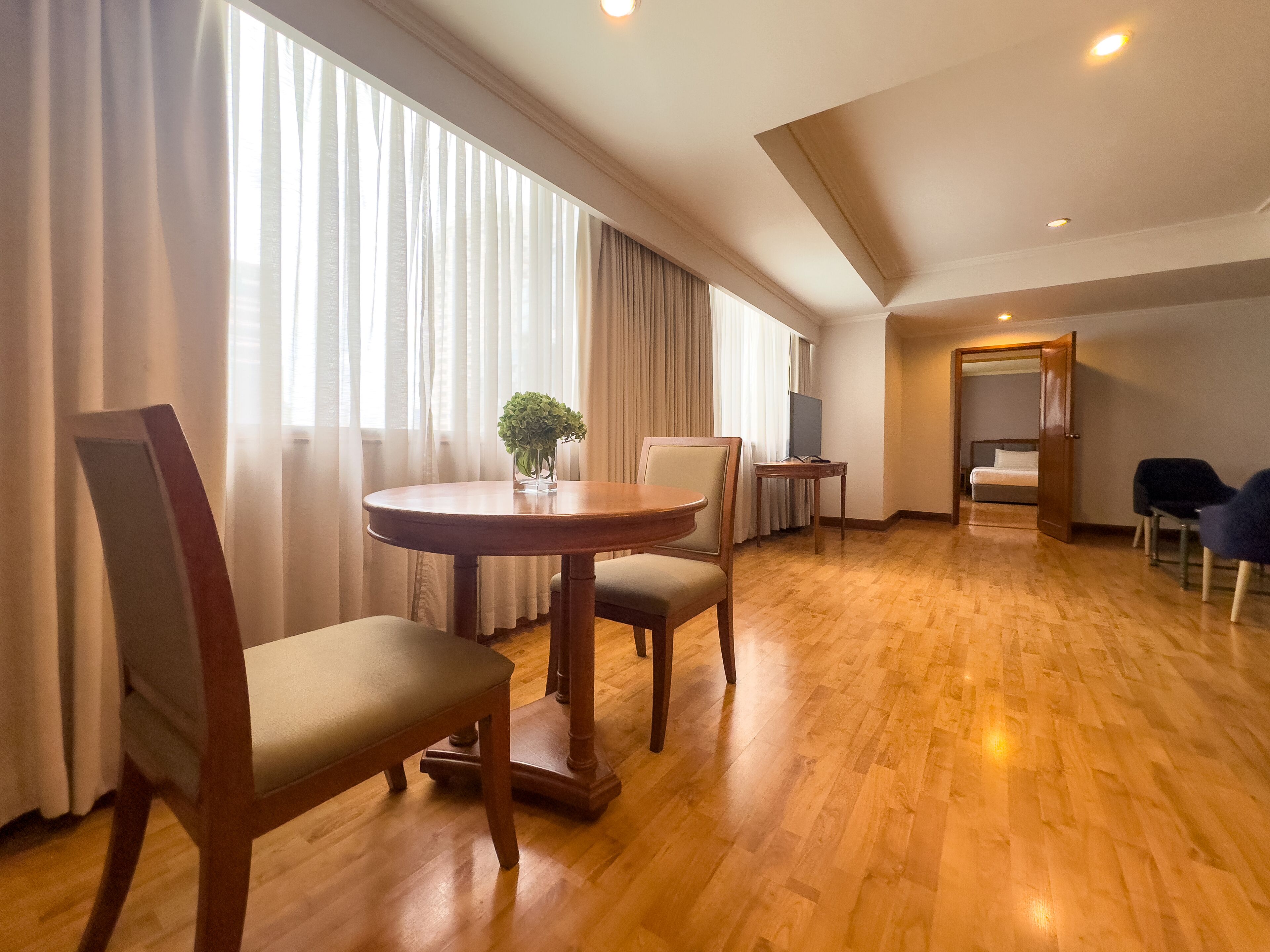 A spacious room with a wooden floor, a round table with chairs, a bed, and a TV.