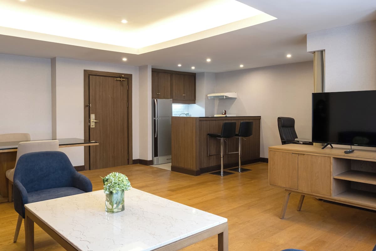 Una sala de estar moderna con una mesa de centro de mármol, televisión y una zona de cocina con refrigerador y taburetes de bar.