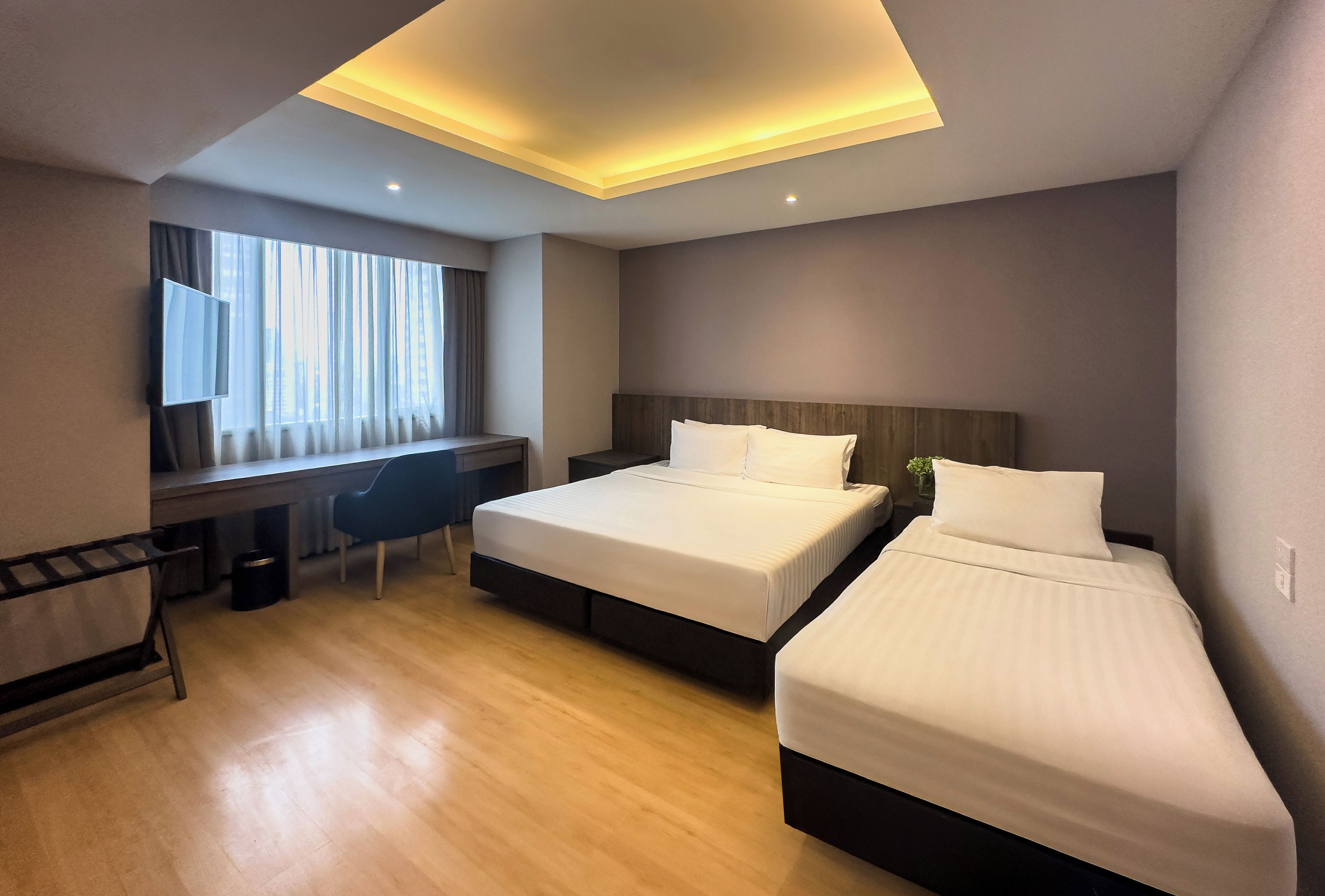 Ein Hotelzimmer mit zwei Betten, einem Schreibtisch, einem Sessel und einem Fernseher.