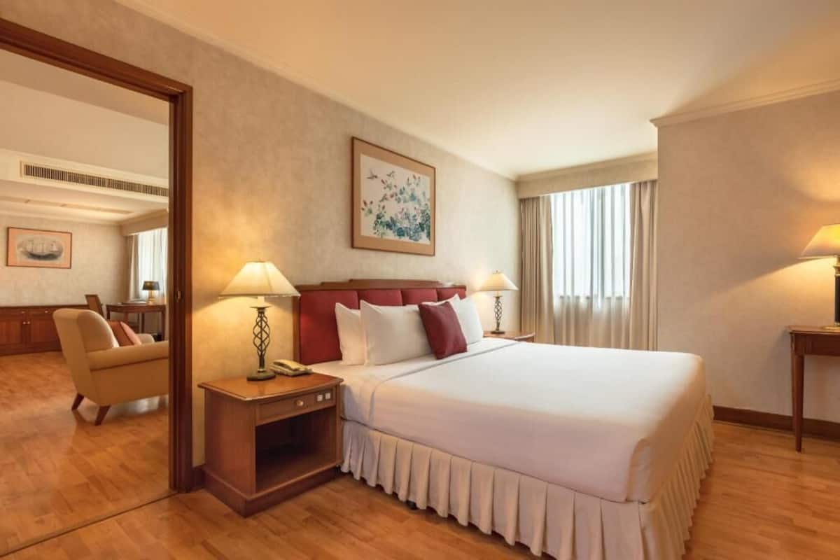 Una habitación de hotel con una cama grande, dos mesitas de noche con lámparas, una silla, un espejo y un cuadro en la pared.