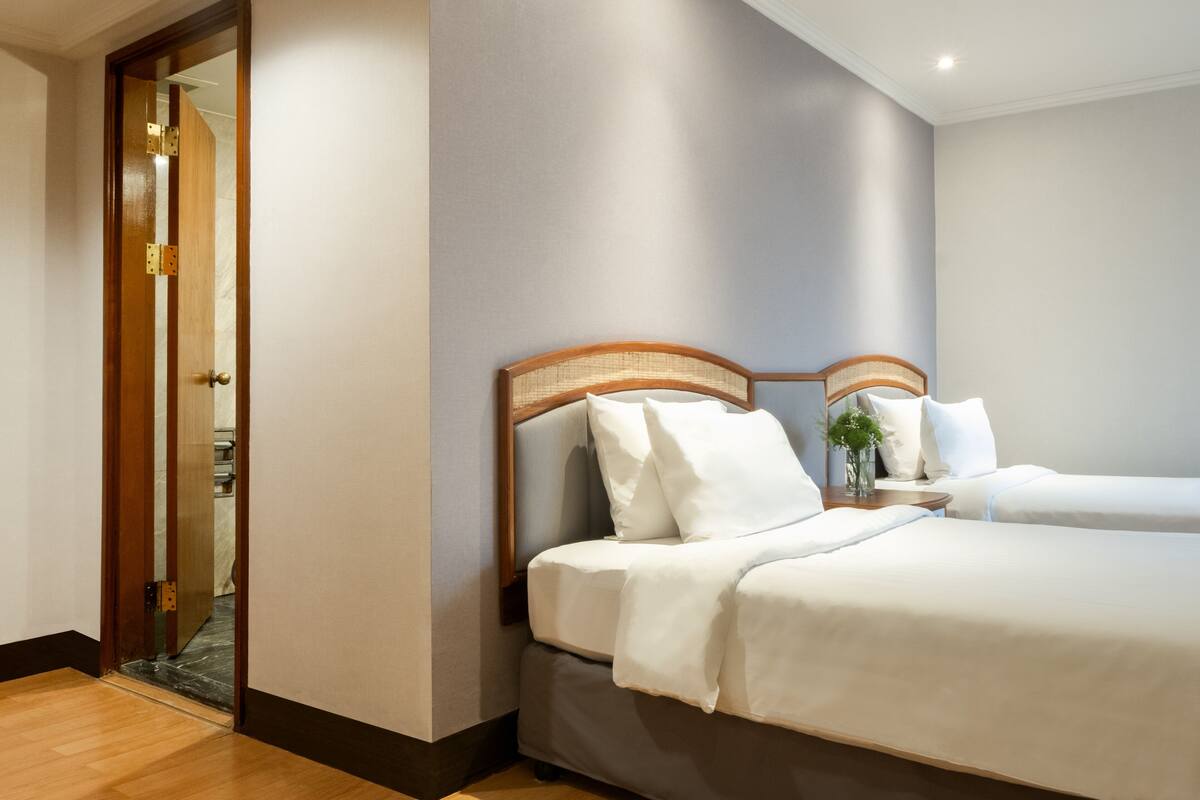 Habitación de hotel con una cama grande, una mesita de noche con un florero y una puerta de madera con espejo.