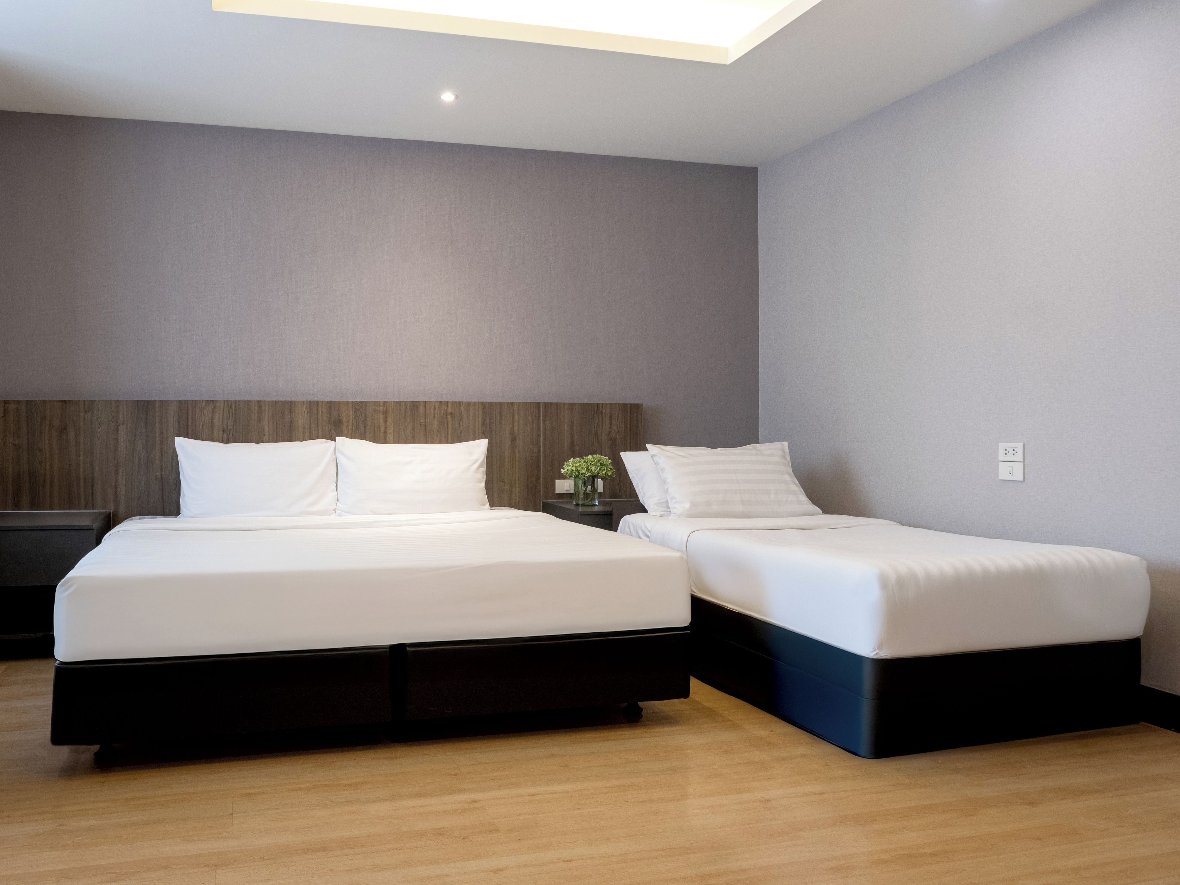 Een moderne hotelkamer met twee bedden, een houten hoofdbord, een klein nachtkastje met een vaas en een plafondlamp.