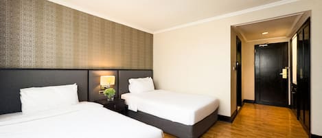 Habitación de hotel con dos camas, una mesita de noche con lámpara y suelo de madera.