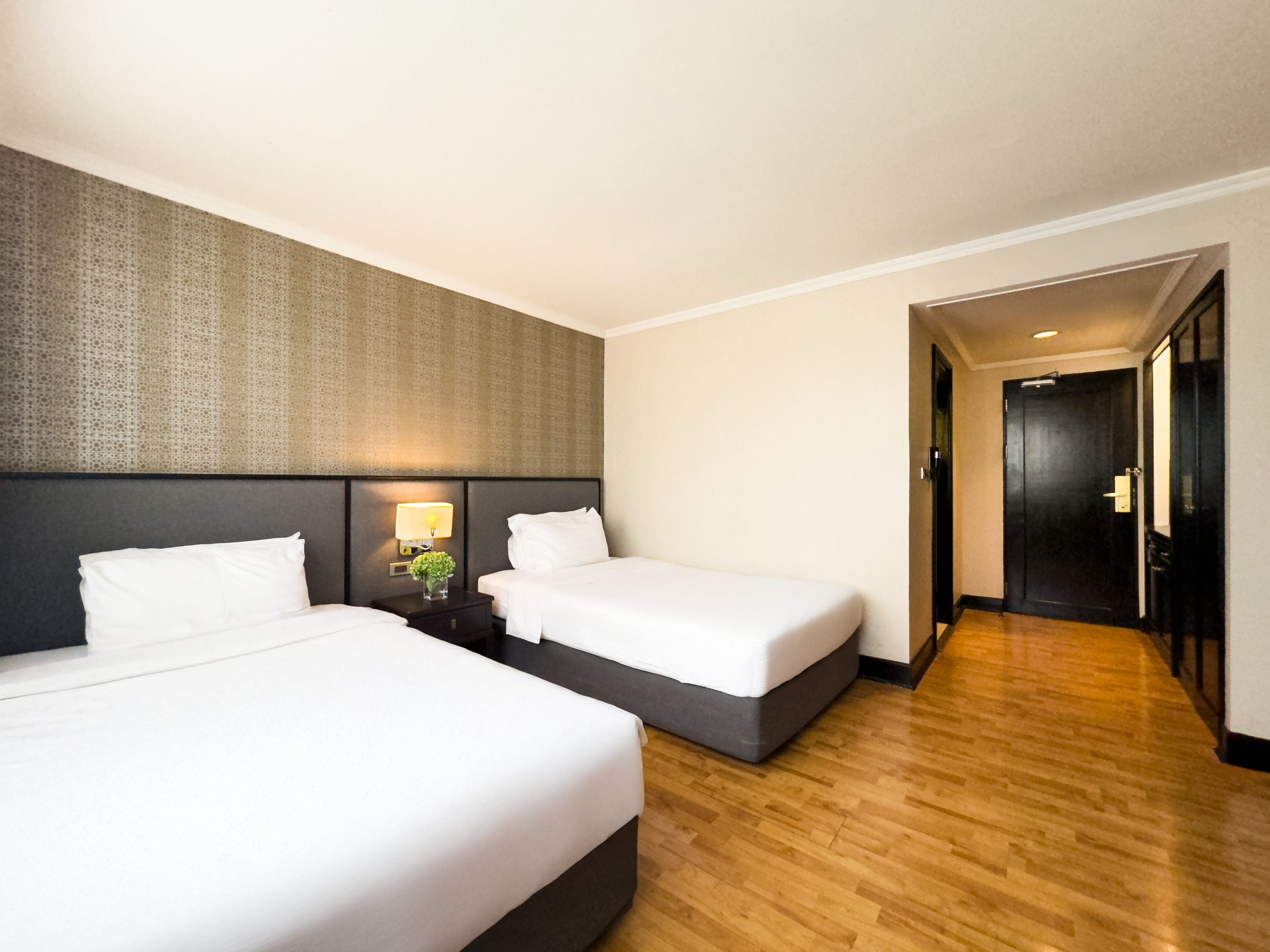 A hotel room with two beds, a nightstand with a lamp, and a wooden floor.