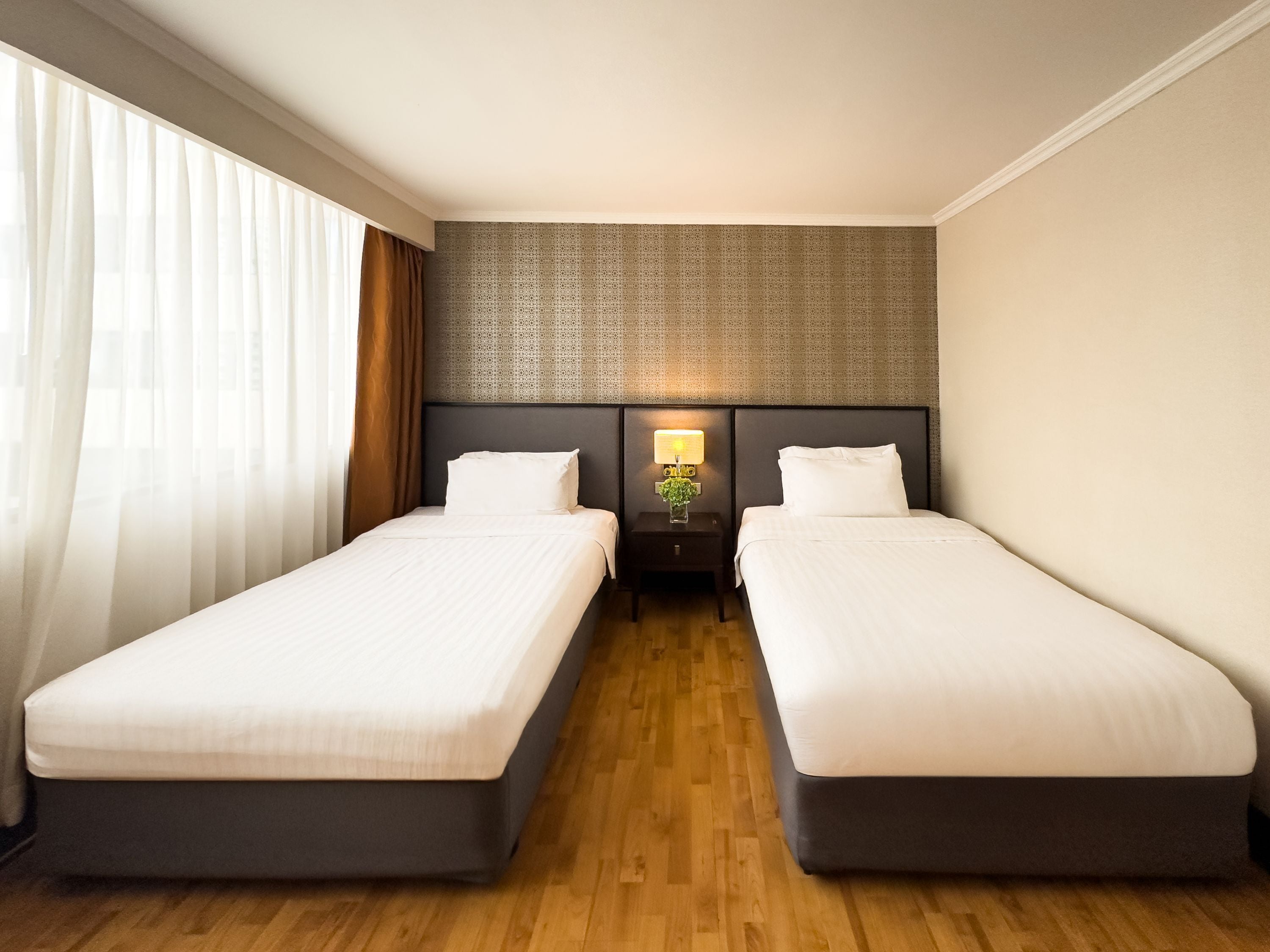 A hotel room with two single beds, a nightstand with a lamp, and a patterned headboard.