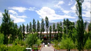A hotel entrance with a paved pathway leading to a building, surrounded by trees and a clear sky. - TIH Global Family Resort - Saboo - Leh (Leh)