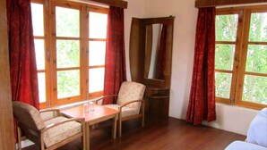 A room with wooden flooring, a wooden table with two chairs, a mirror, and large windows with red curtains. - TIH Global Family Resort - Saboo - Leh (Leh)