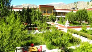 A building with a red roof and white walls, surrounded by lush greenery and mountains in the background. - TIH Global Family Resort - Saboo - Leh (Leh)