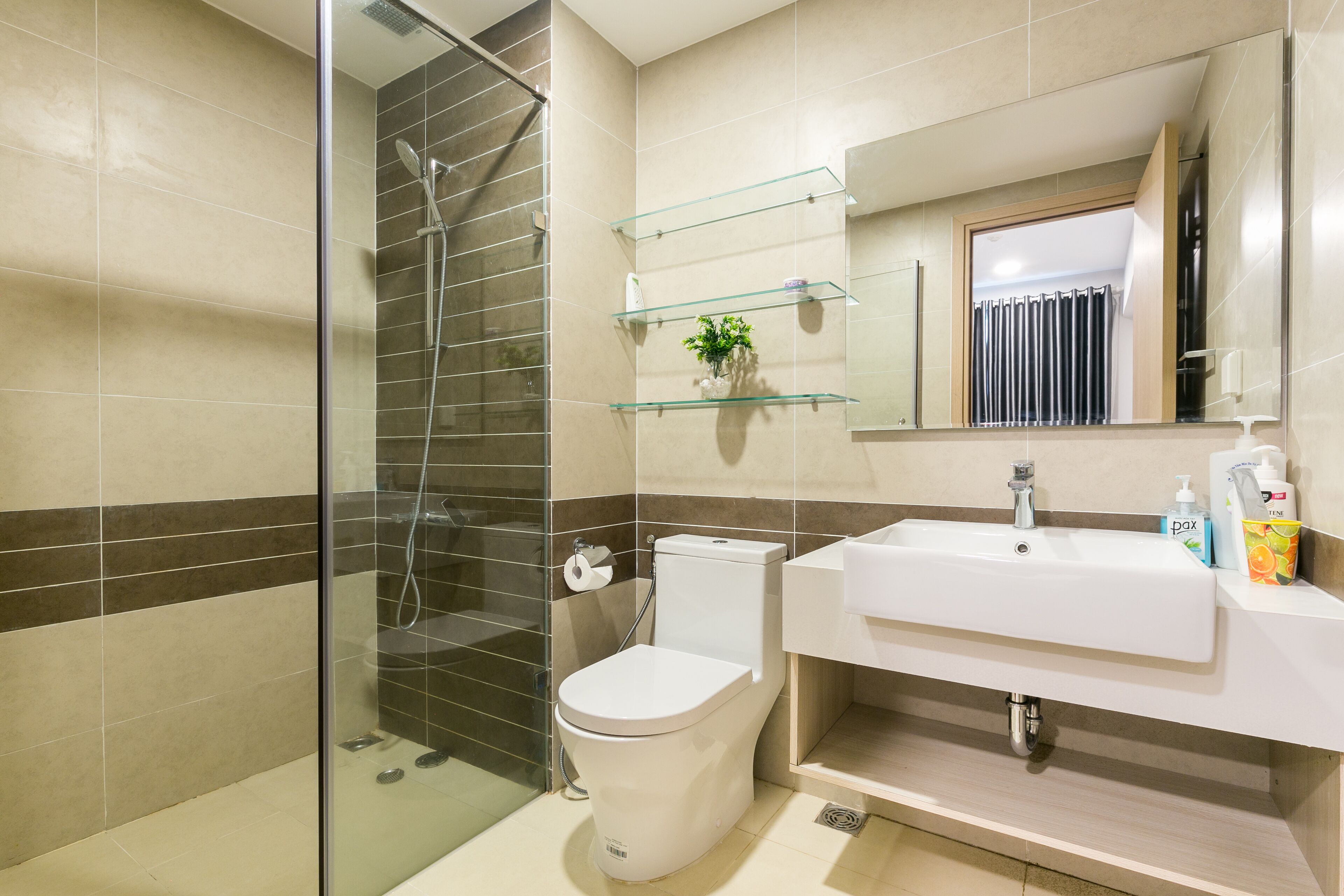Une salle de bain moderne avec une douche à parois de verre, des toilettes blanches et un lavabo surmonté d’un miroir.