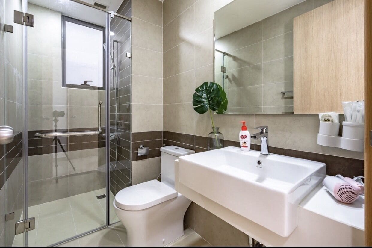 Une salle de bain moderne avec une douche à parois de verre, des toilettes blanches, un grand lavabo avec un miroir et un meuble en bois au-dessus du lavabo.