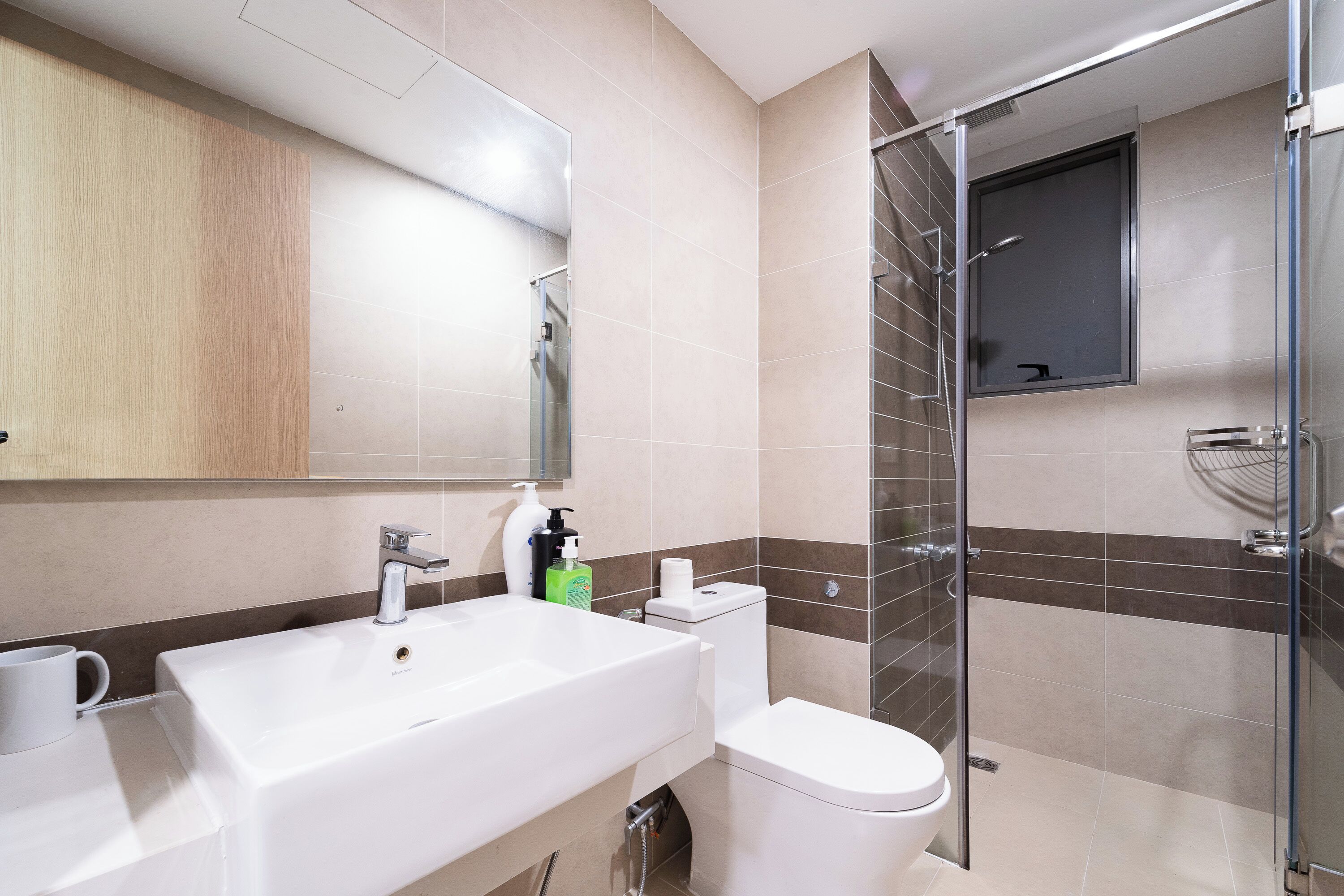 A modern bathroom with a large mirror, a sink, a toilet, and a glass-enclosed shower.
