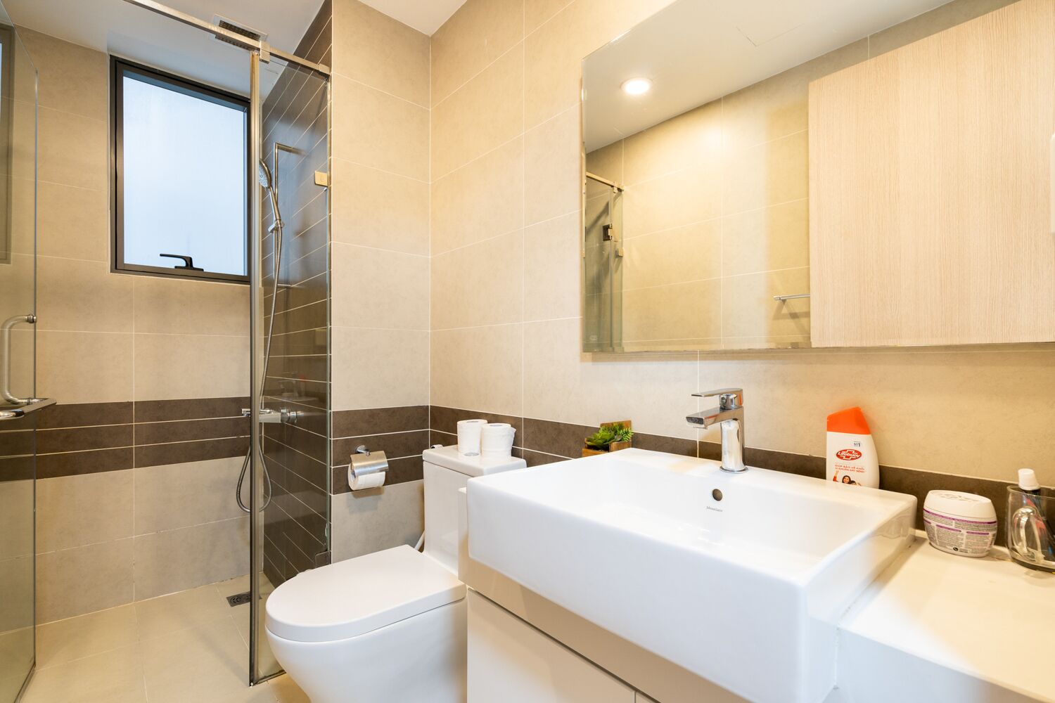 Une salle de bain moderne avec une douche à parois de verre, des toilettes blanches, un grand lavabo blanc et un miroir au-dessus du lavabo.