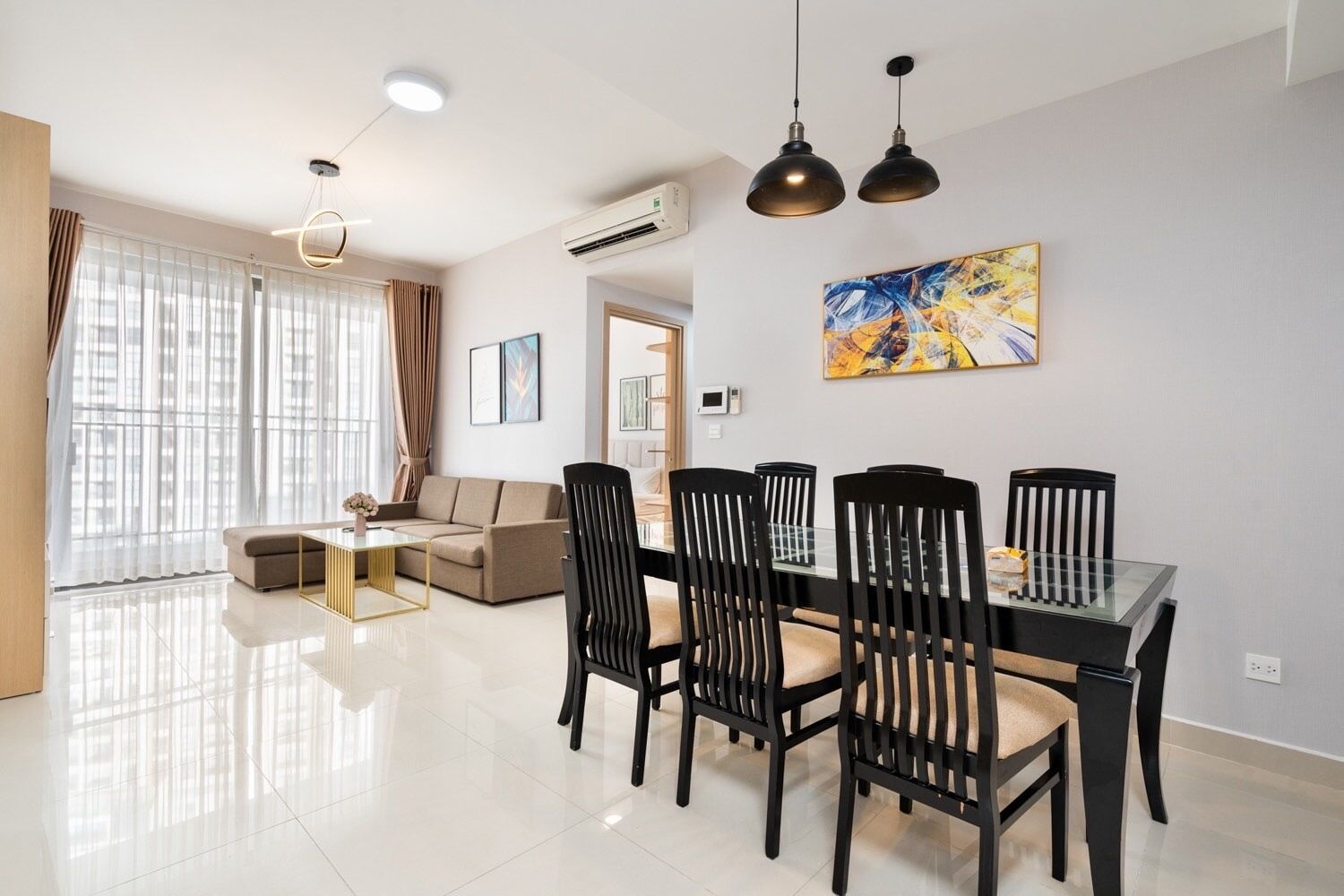 A modern living room with a dining area, featuring a sofa, a glass-top dining table with black chairs, and a large abstract painting on the wall.