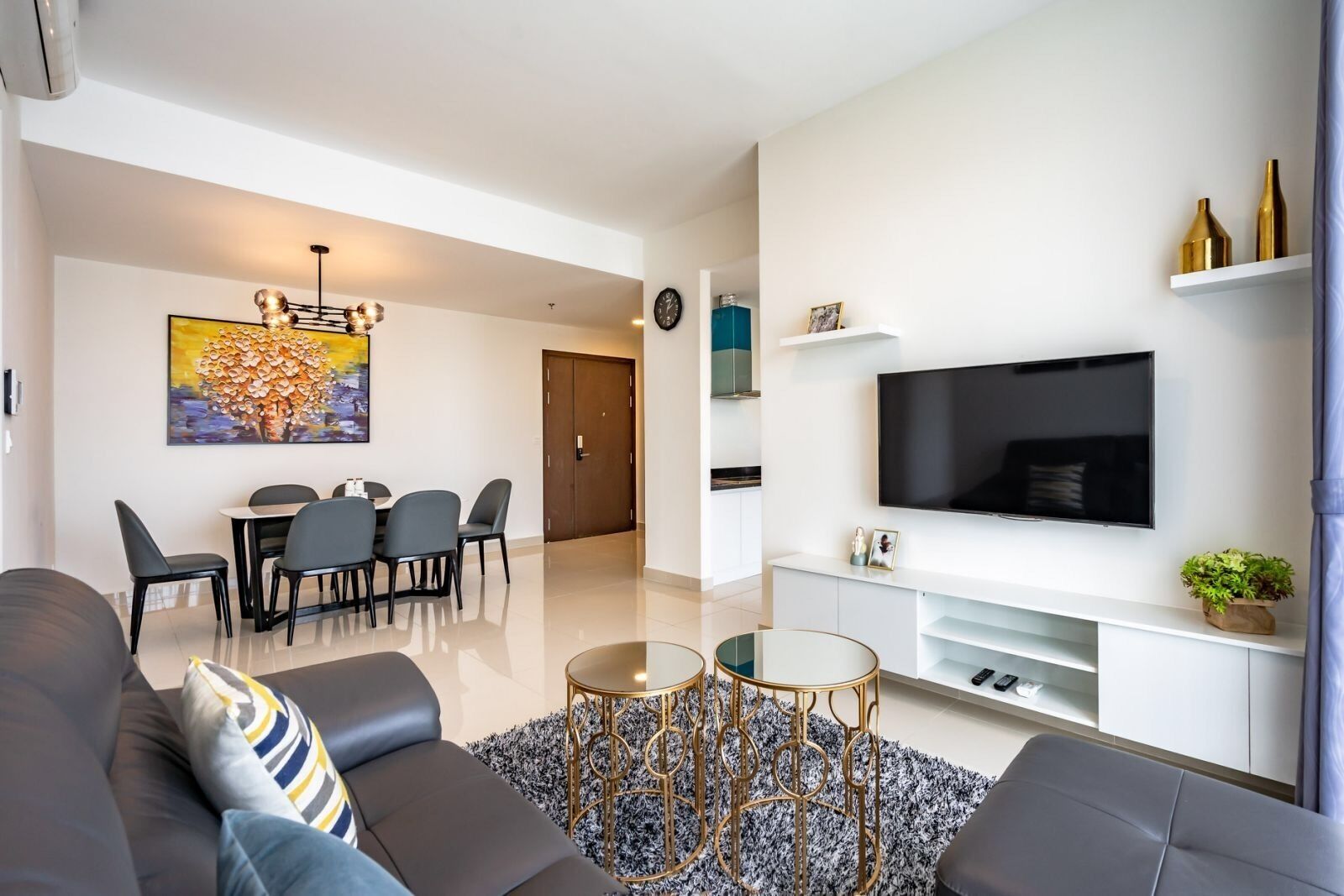 Un soggiorno moderno con un divano, un tavolo da pranzo con sedie, un televisore su un mobile bianco e una sveglia appesa al muro.