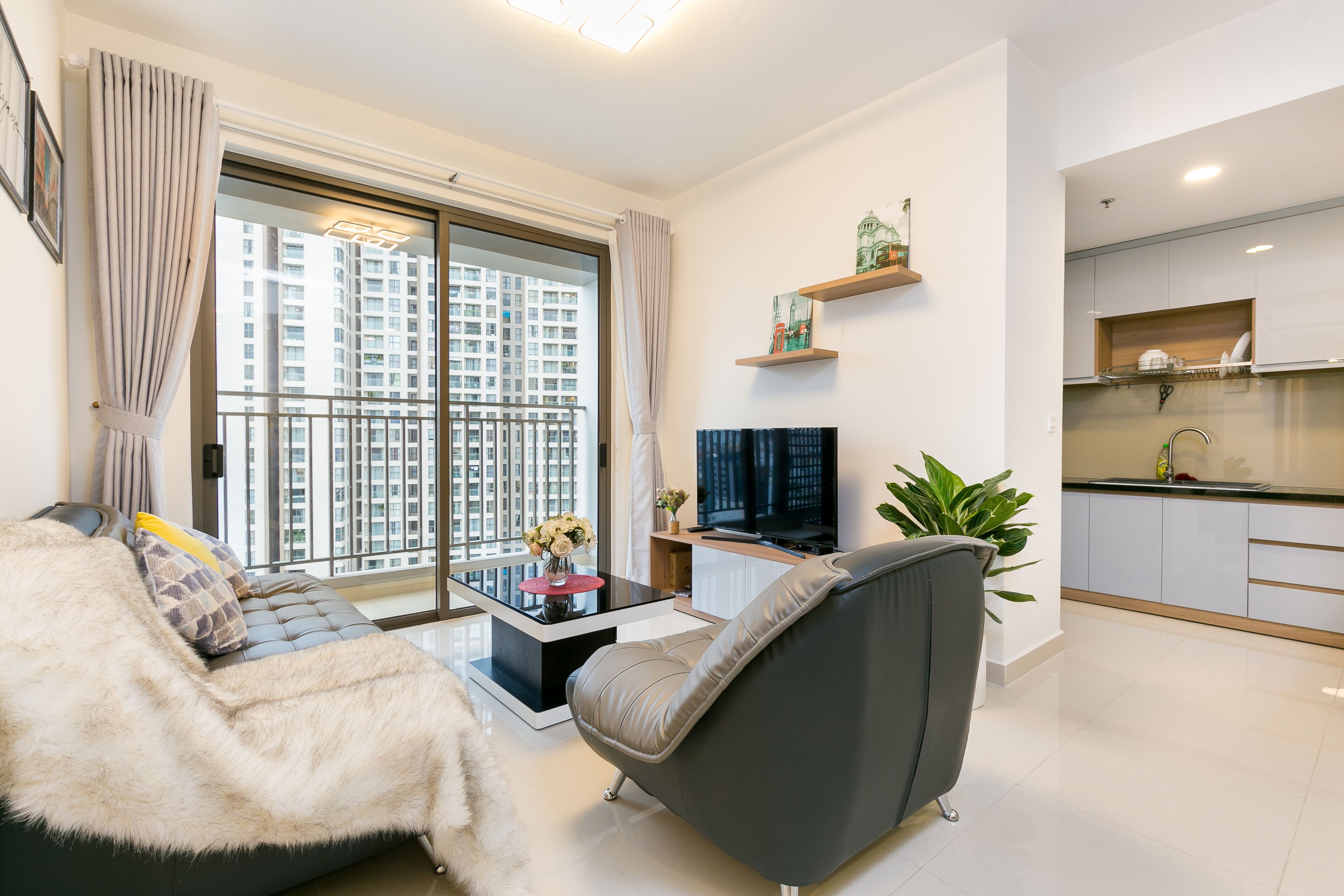Una sala de estar moderna con un sofá, una mesa de centro, un televisor y un balcón con cortinas.