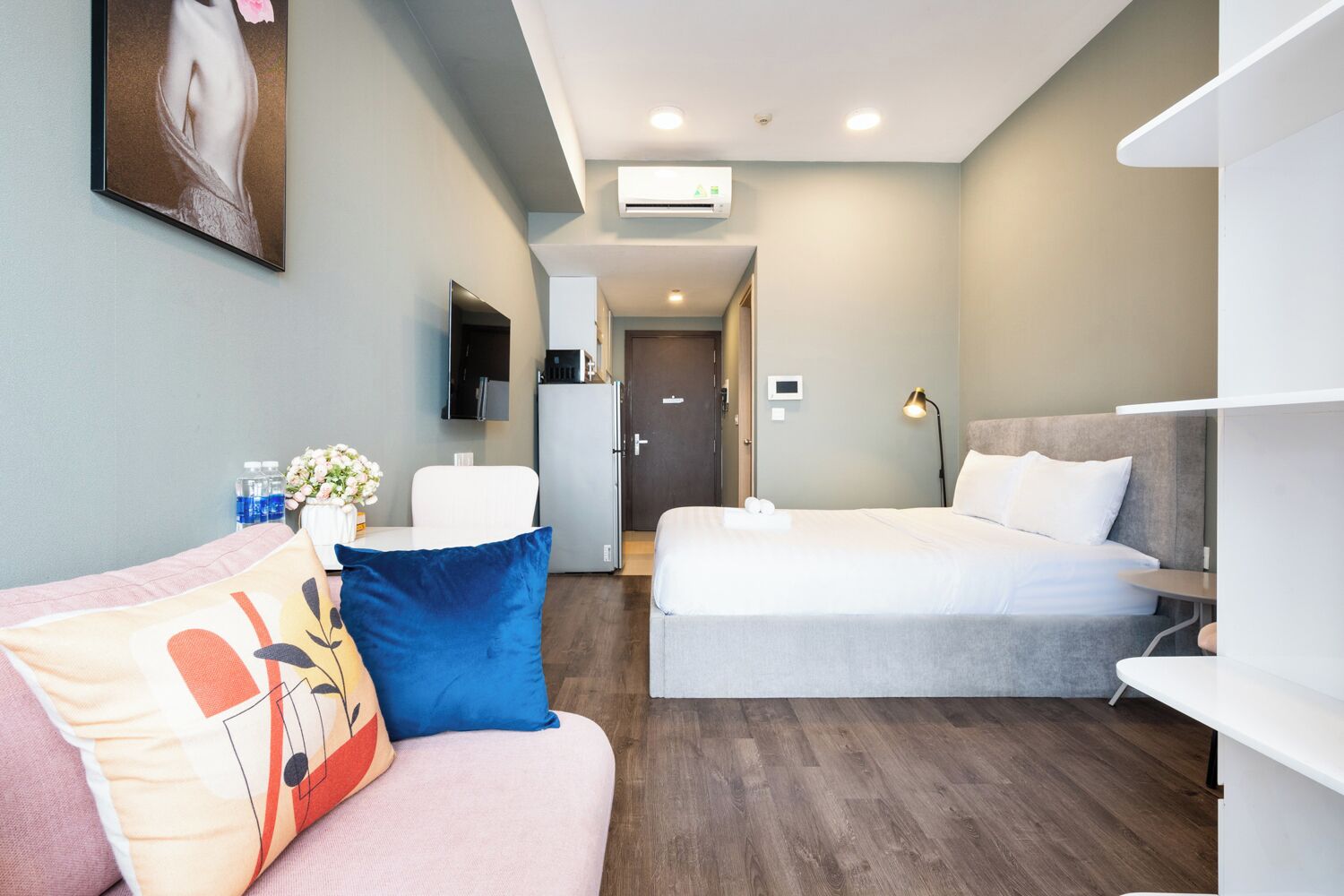 Een moderne hotelkamer met een bank, twee bedden, een televisie, een bureau en een badkamer op de achtergrond.