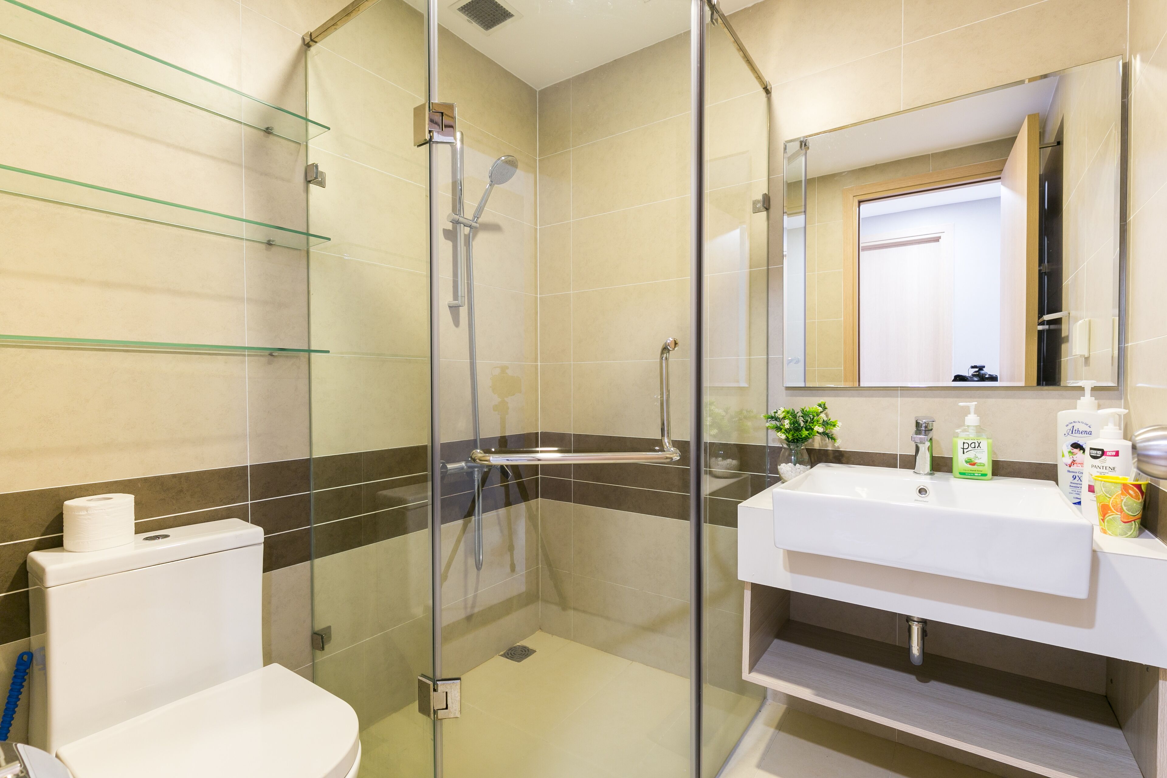 A modern bathroom with a glass-enclosed shower, a white sink with toiletries, and a toilet.