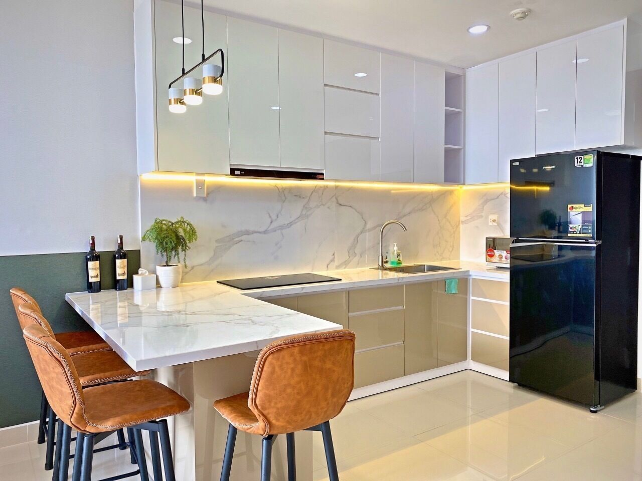 Uma cozinha moderna com bancadas de mármore branco, uma geladeira preta e duas cadeiras de couro marrom.