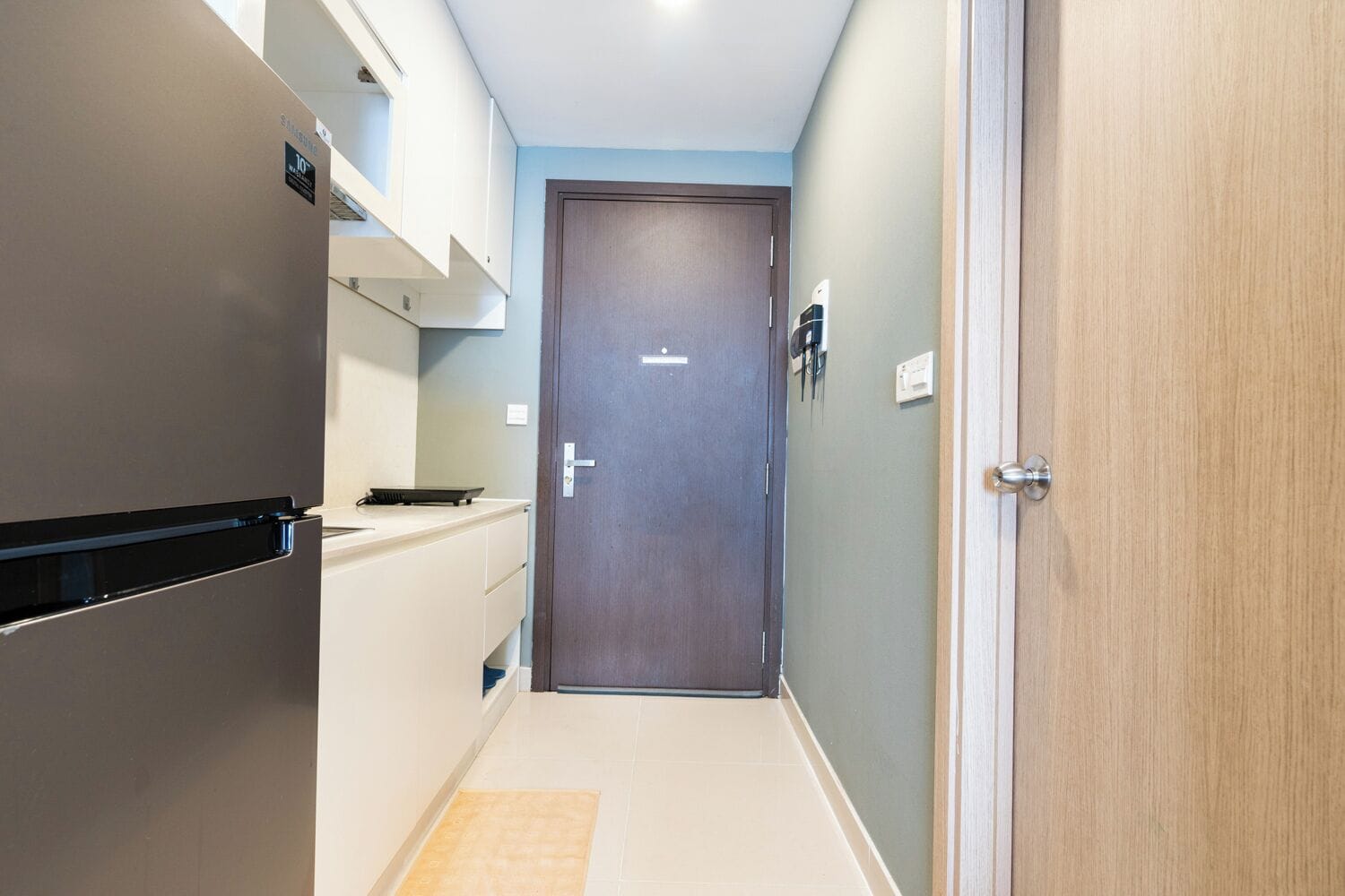 Un pasillo estrecho con un refrigerador, un microondas y una pequeña encimera de cocina.