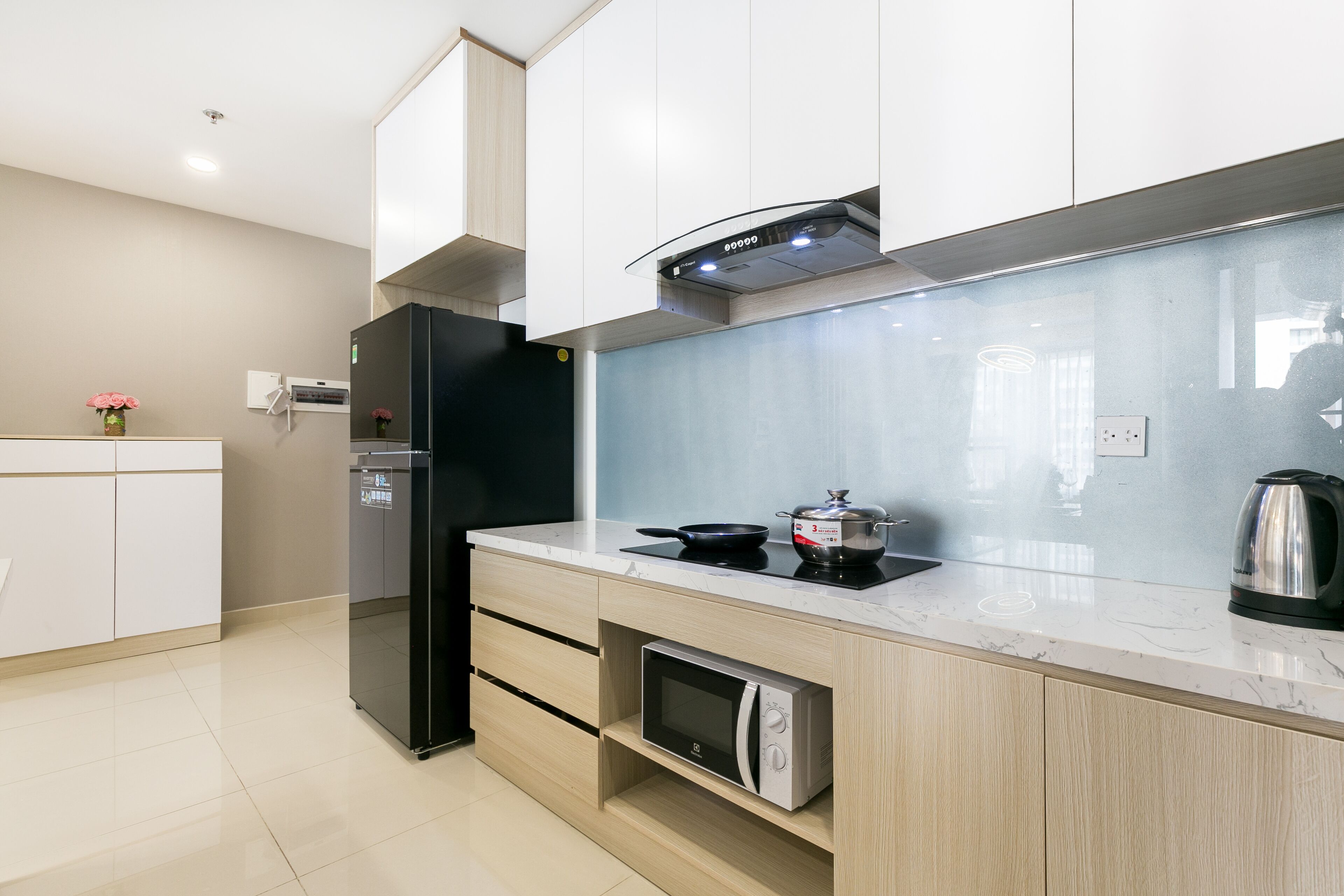 Una cocina moderna con microondas integrado, un refrigerador negro y un hervidor de acero inoxidable sobre la encimera.