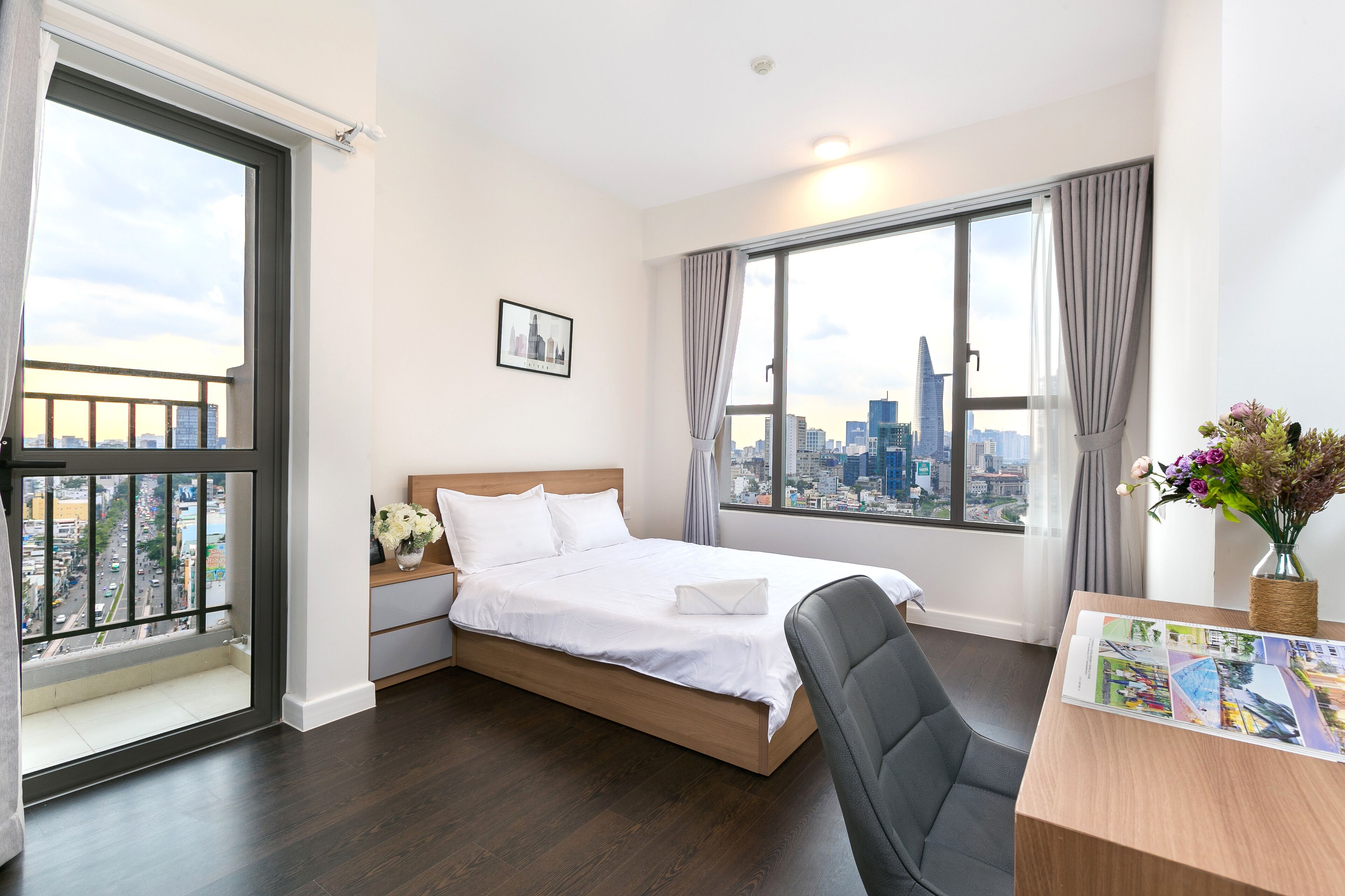 A modern hotel room with a large bed, a desk with a chair, a city view, and a window with curtains.
