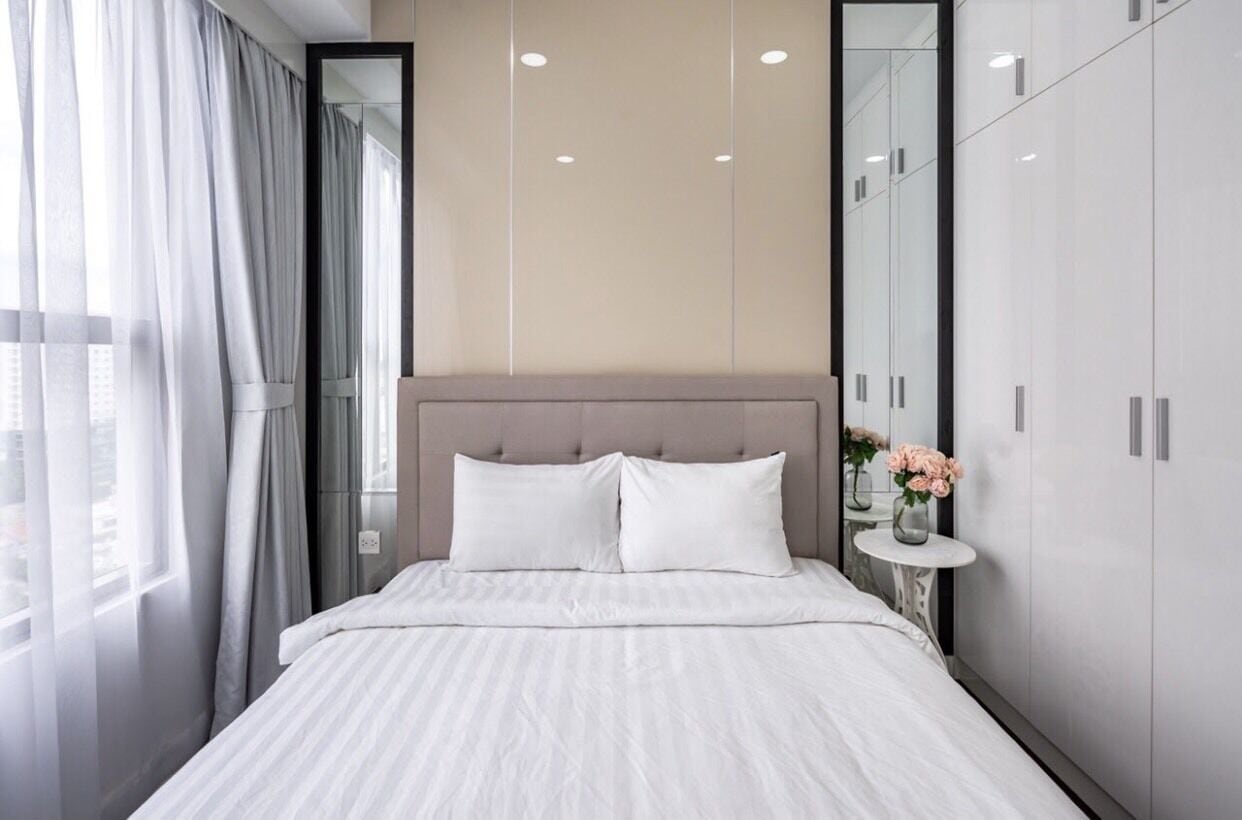 Un dormitorio moderno con una cama grande, un cabecero, una mesita de noche con un jarrón y un armario.