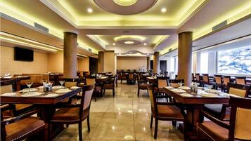 A spacious dining area with multiple tables and chairs, a modern ceiling design, and large windows.