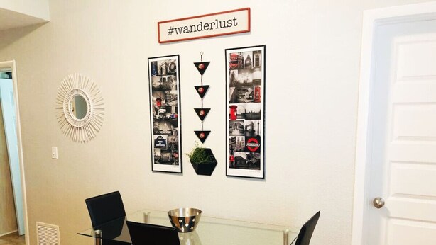 Een eethoek met een glazen tafel en zwarte stoelen, een decoratieve spiegel en ingelijste foto's aan de wand.