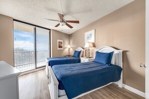 A bedroom with two beds, a ceiling fan, a nightstand with a lamp, and a window with blinds. - Sea Gull #404: Beachfront 2 Bedroom 2 Bath with Spectacular Views and 24 Hour Management (Port Aransas)