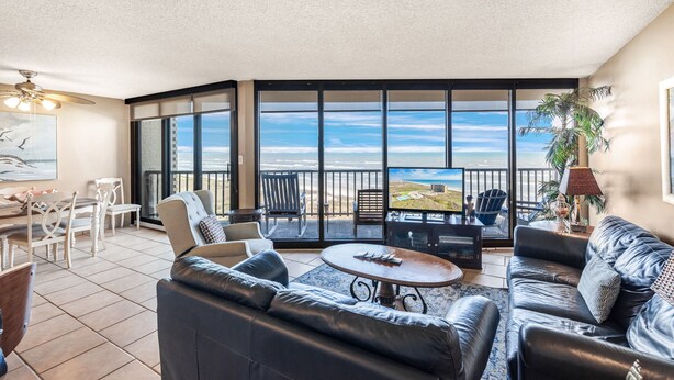 A spacious living room with a large window, a leather sofa, a dining area, and a balcony with a view.